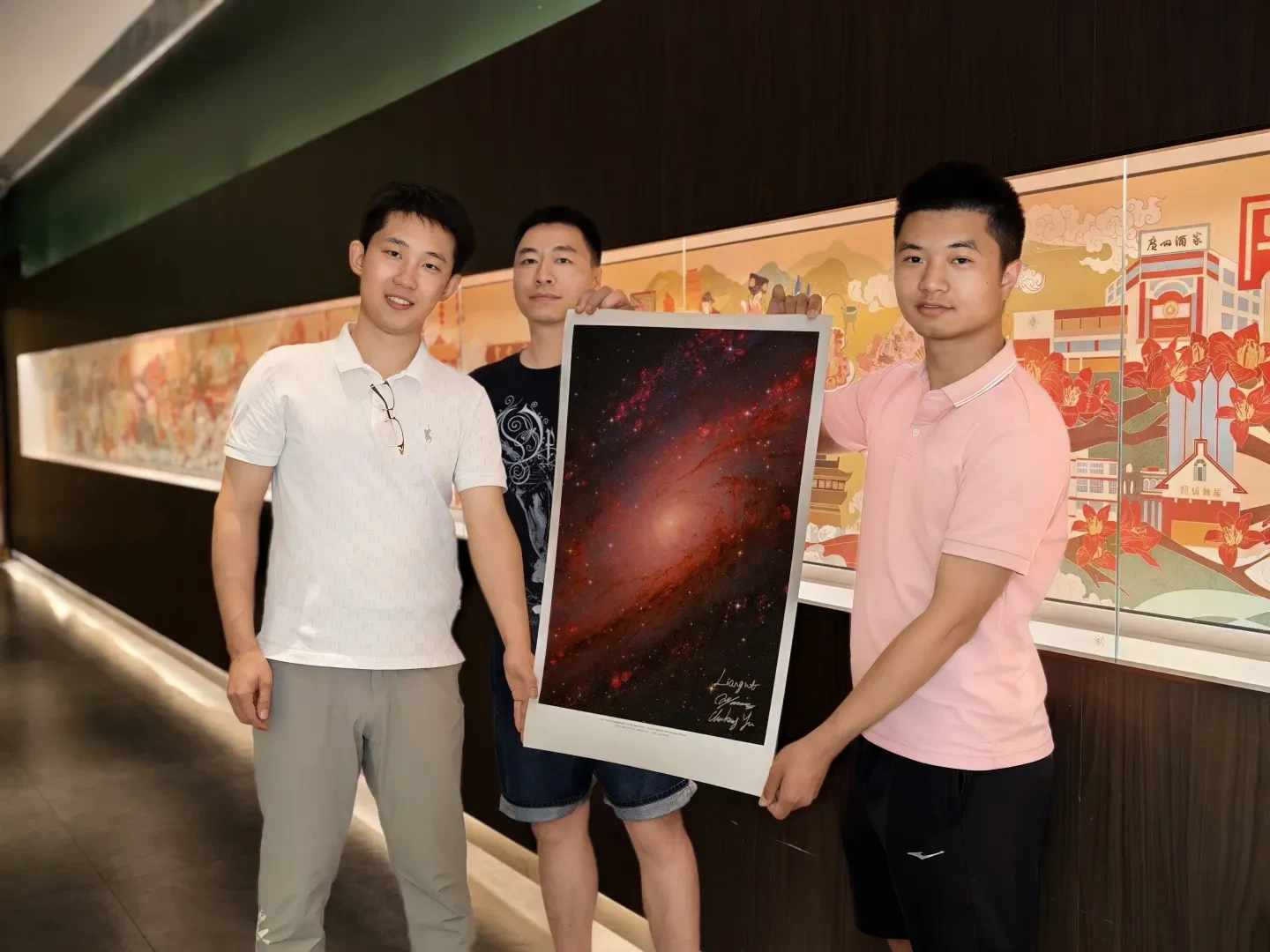 Photo of three men holding up a large print of a galaxy