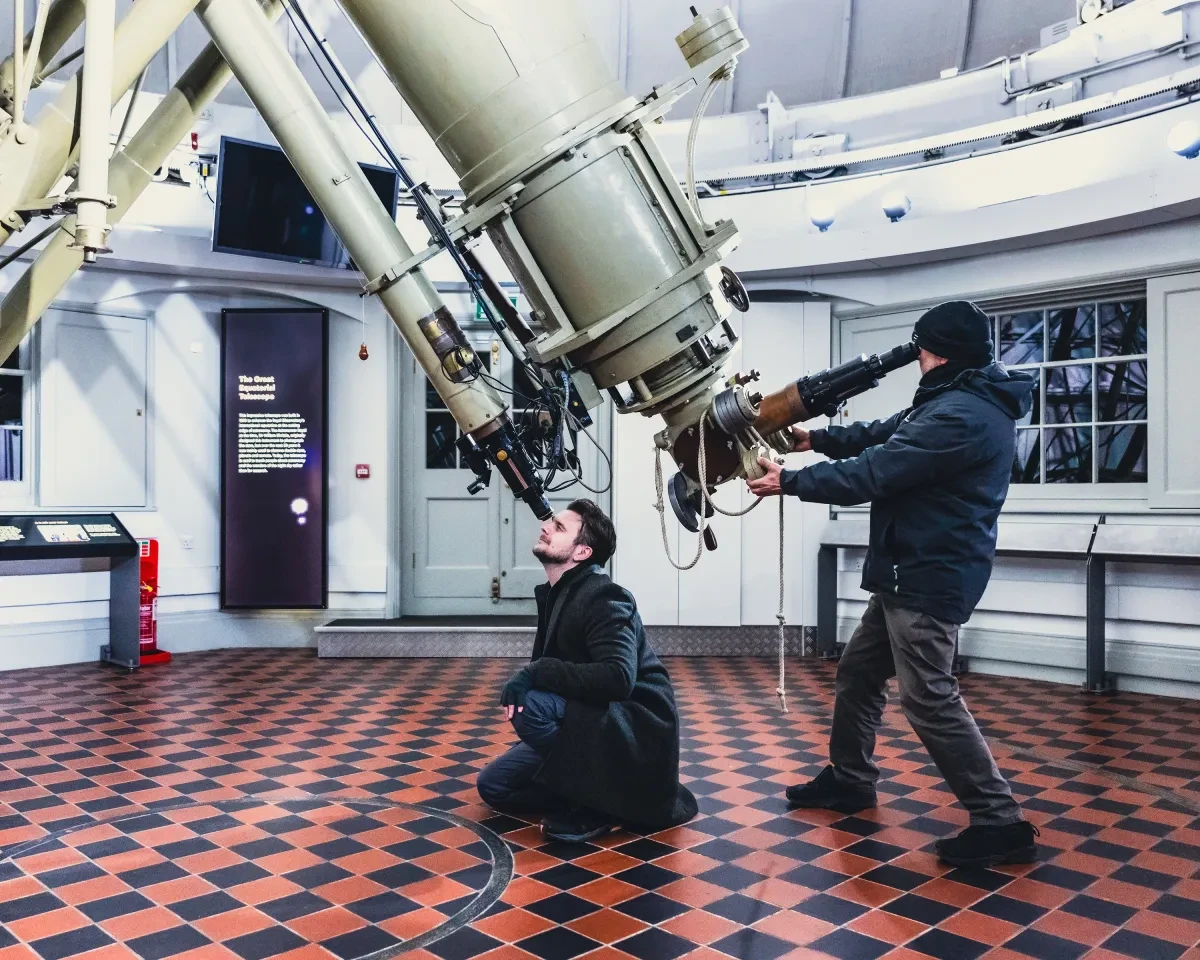 An astronomer kneels to look through the eyepiece of the Great Equatorial Telescope at Royal Observatory Greenwich