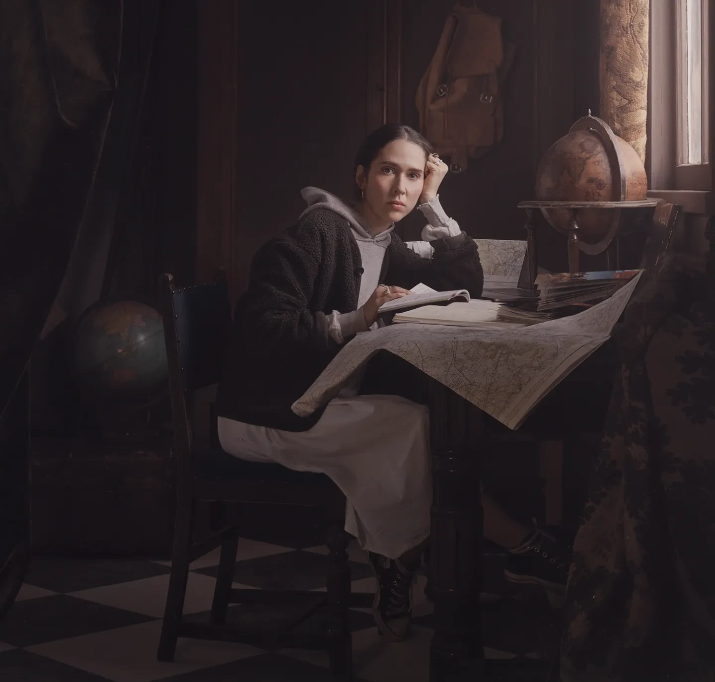 A woman sits at a desk reminiscent of a 17th century painting wearing modern clothes