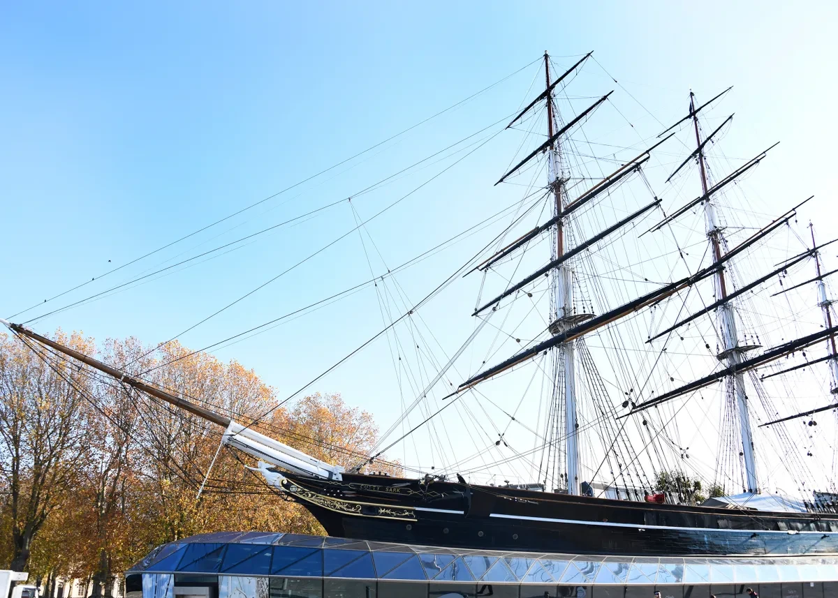 Exterior view of Cutty Sark in the sun. The masts of the ship are silhouetted against a bright blue sky.