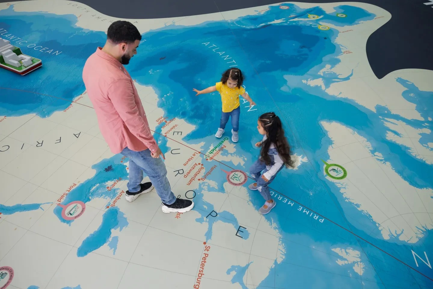 A father and two young daughters play on the Ocean Map, a giant floor map of the world, at the National Maritime Museum.