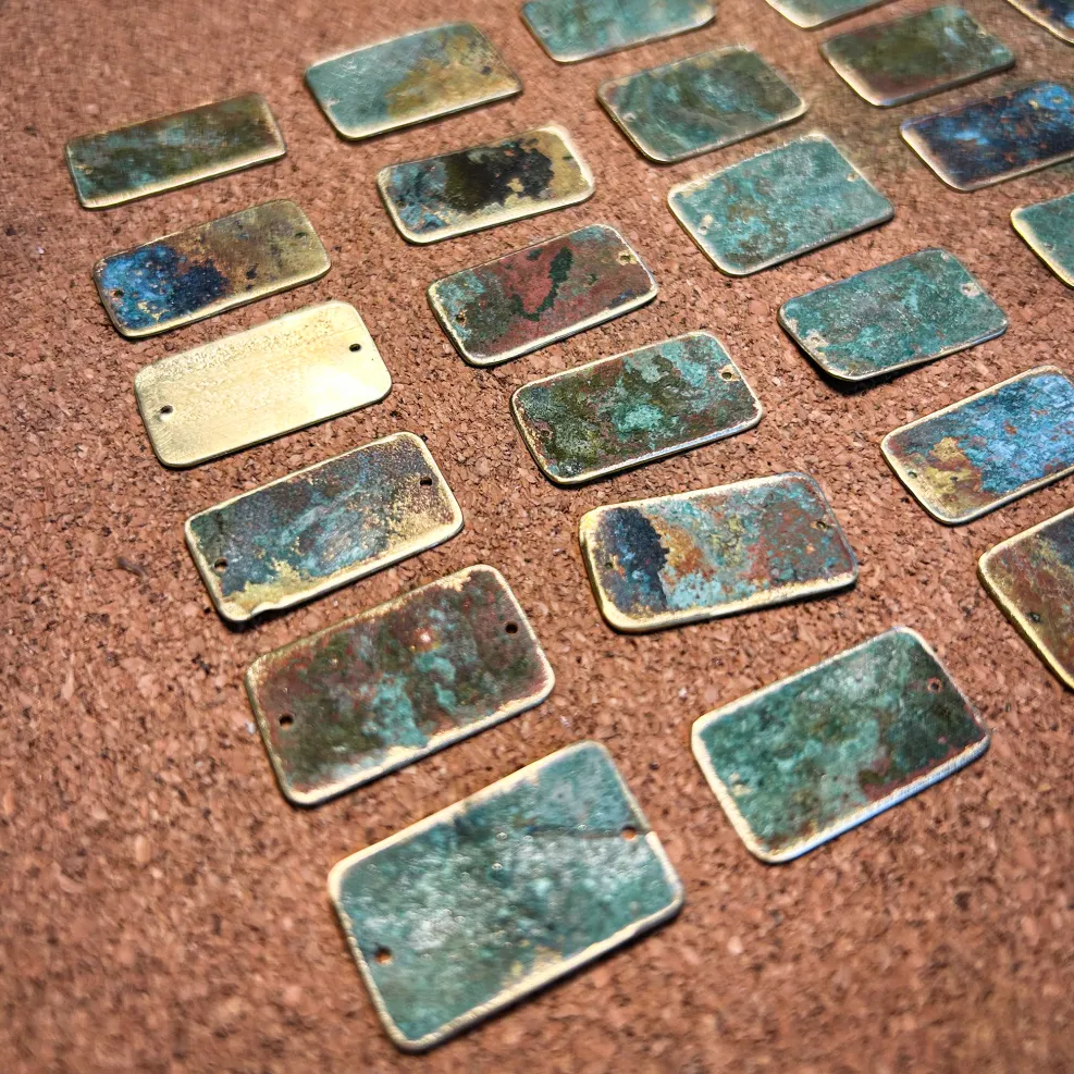 A set of small pieces of rectangular metal on a workbench. The metal has a worn patina, with blue and orange discolouration on the shiny surface