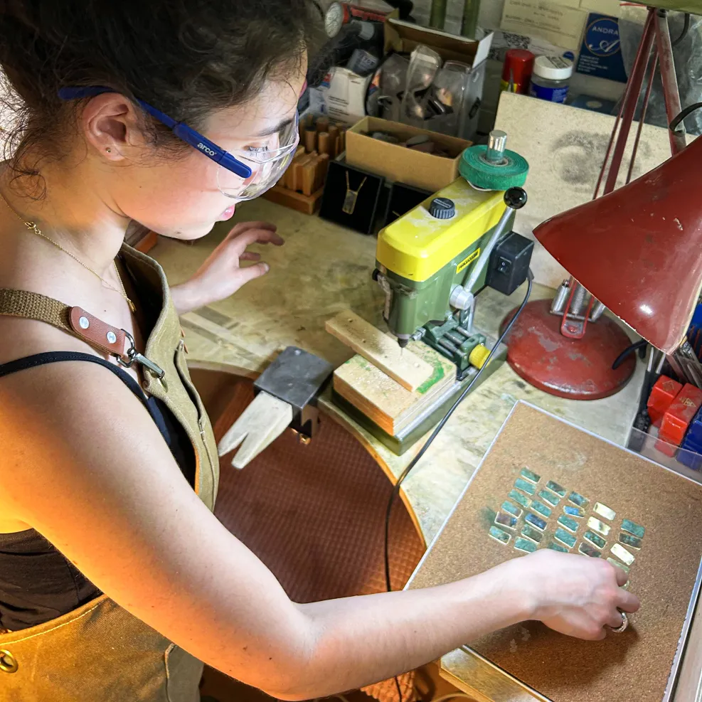 A woman examines a set of small rectangular metal rectangles on a workbench