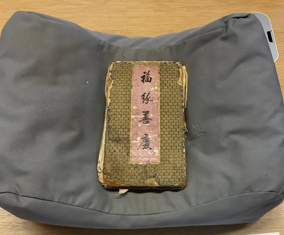 A manuscript item laying on a support pillow. There are four Chinese characters printed on the cover. 