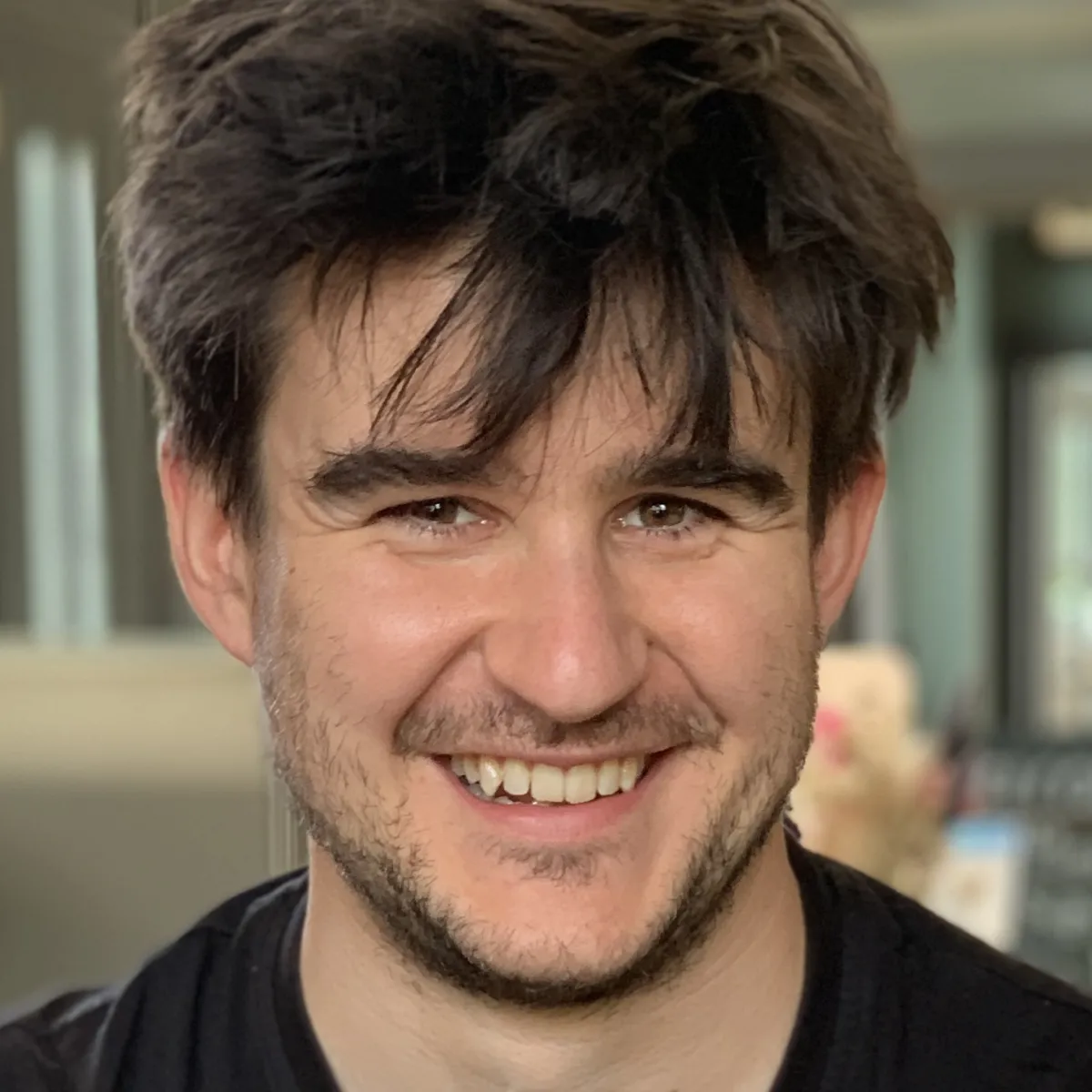 Profile photo showing a man with dark brown hair and light stubble smiling