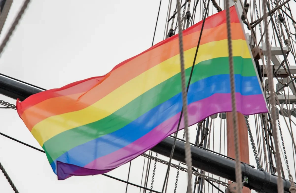 A rainbow flag flies amongst ship rigging.