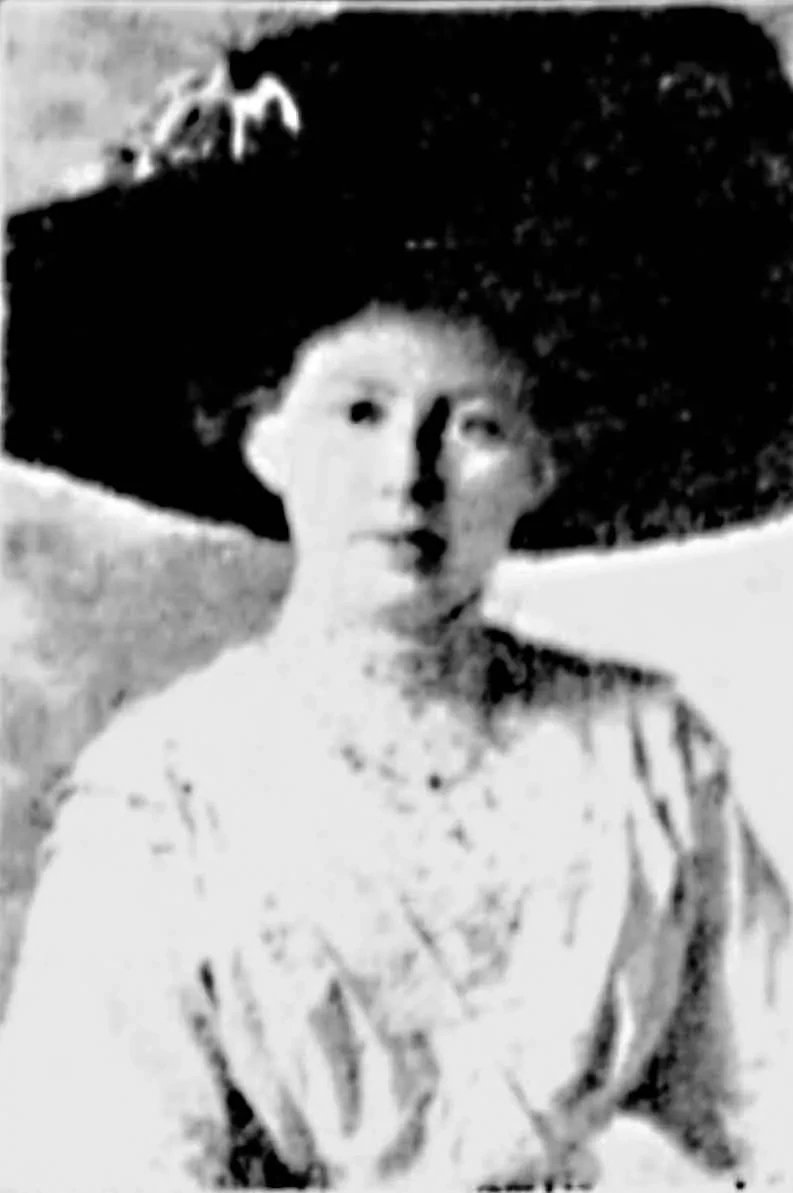 Grainy historical photo of a woman in black and white wearing a large black hat