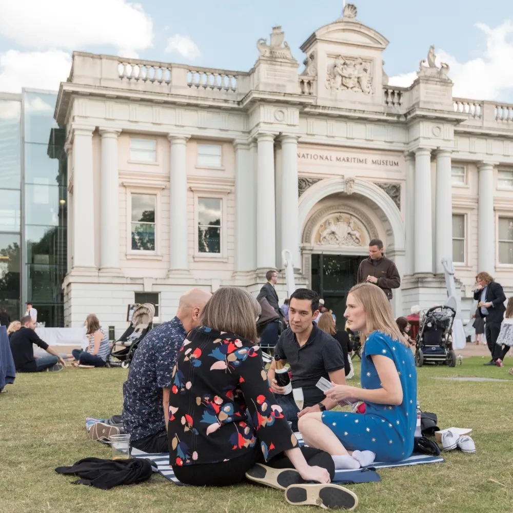 A group of people sitting on the grass in front of the National Maritime Museum.