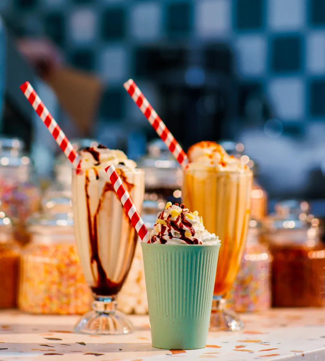 Image of three milkshakes on a counter with colourful toppings and straws
