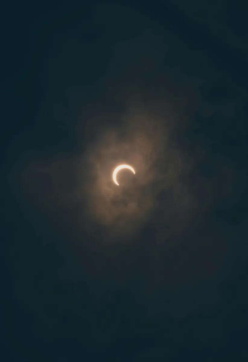 A partial solar eclipse visible through a hazy sky, with the sun appearing as a bright crescent.