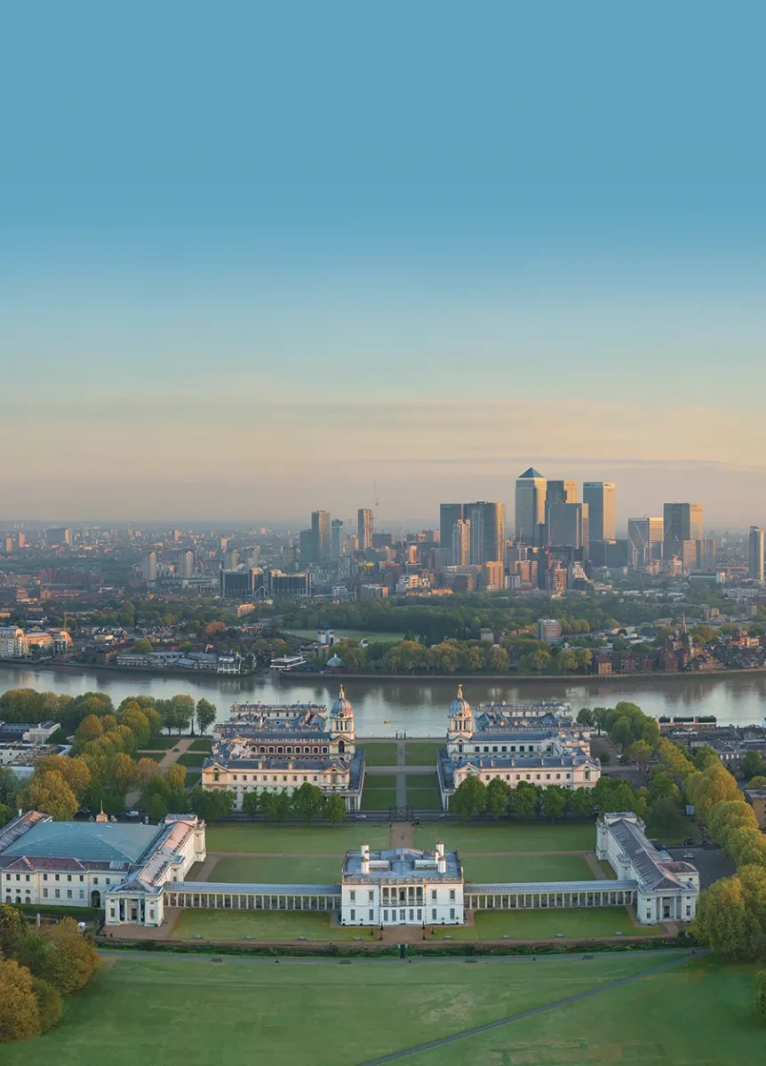 A drone view of historic Greenwich, with the park and museums in the foreground and the towers of Canary Wharf on the horizon