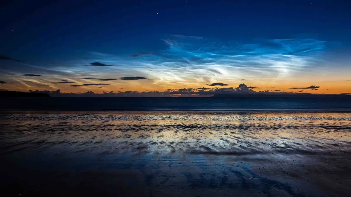 Photograph of clouds reflecting in water at a shoreline at sunset.