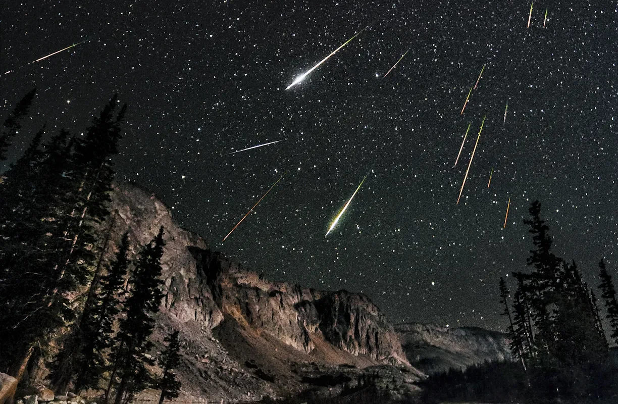 A meteor shower in the black night sky above a mountain range.