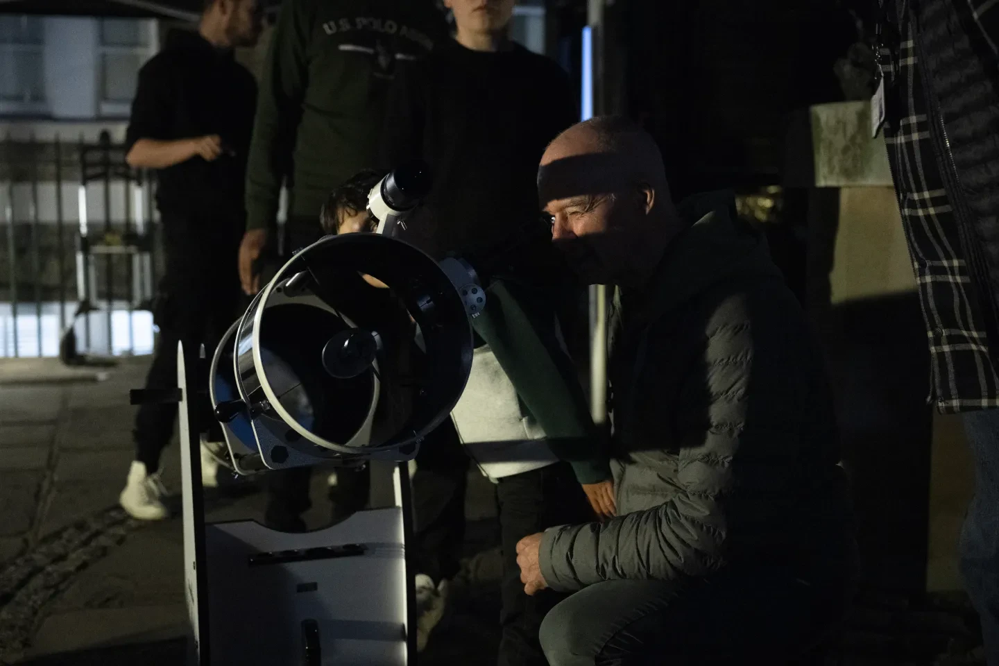 Photo of man crouched down to look through a telescope in a dark location