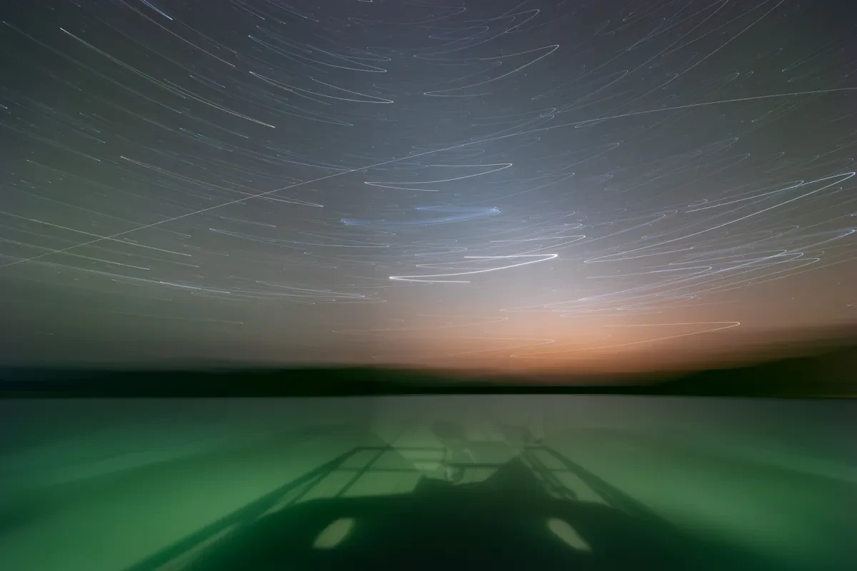 A long exposure reveals streaks of star trails in a dark sky above the vast green ocean.