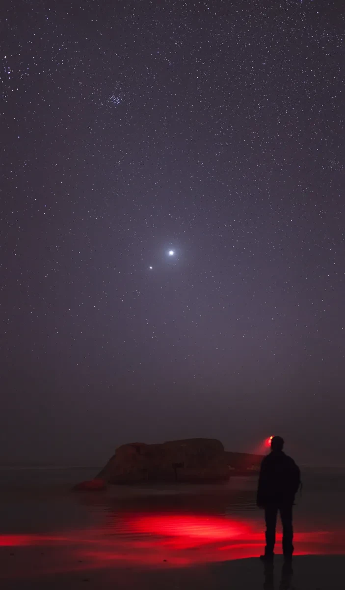 Image of man standing looking at night sky, which has two bright lights close together which are Venus and Jupiter