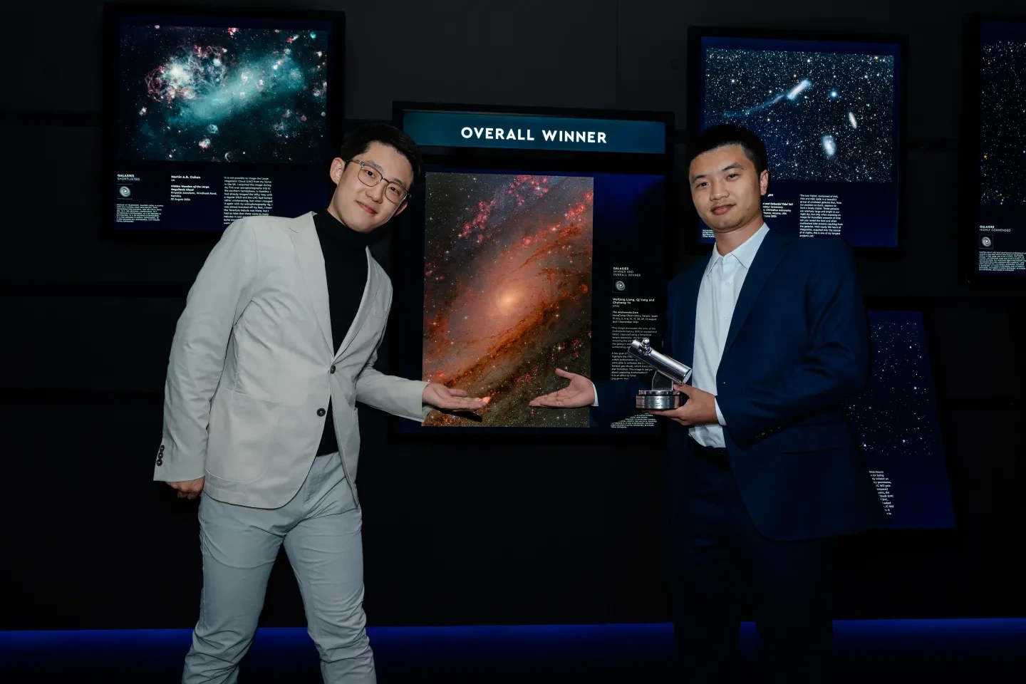 Photo of two photographers standing either side of an image of a red galaxy inside a photography gallery